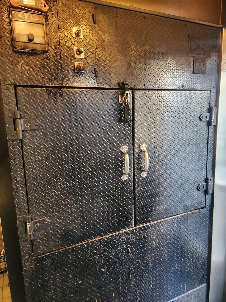 Commercial smoker doors in diamond plate, with an analog temperature gauge and a bank of three switches above the latch.