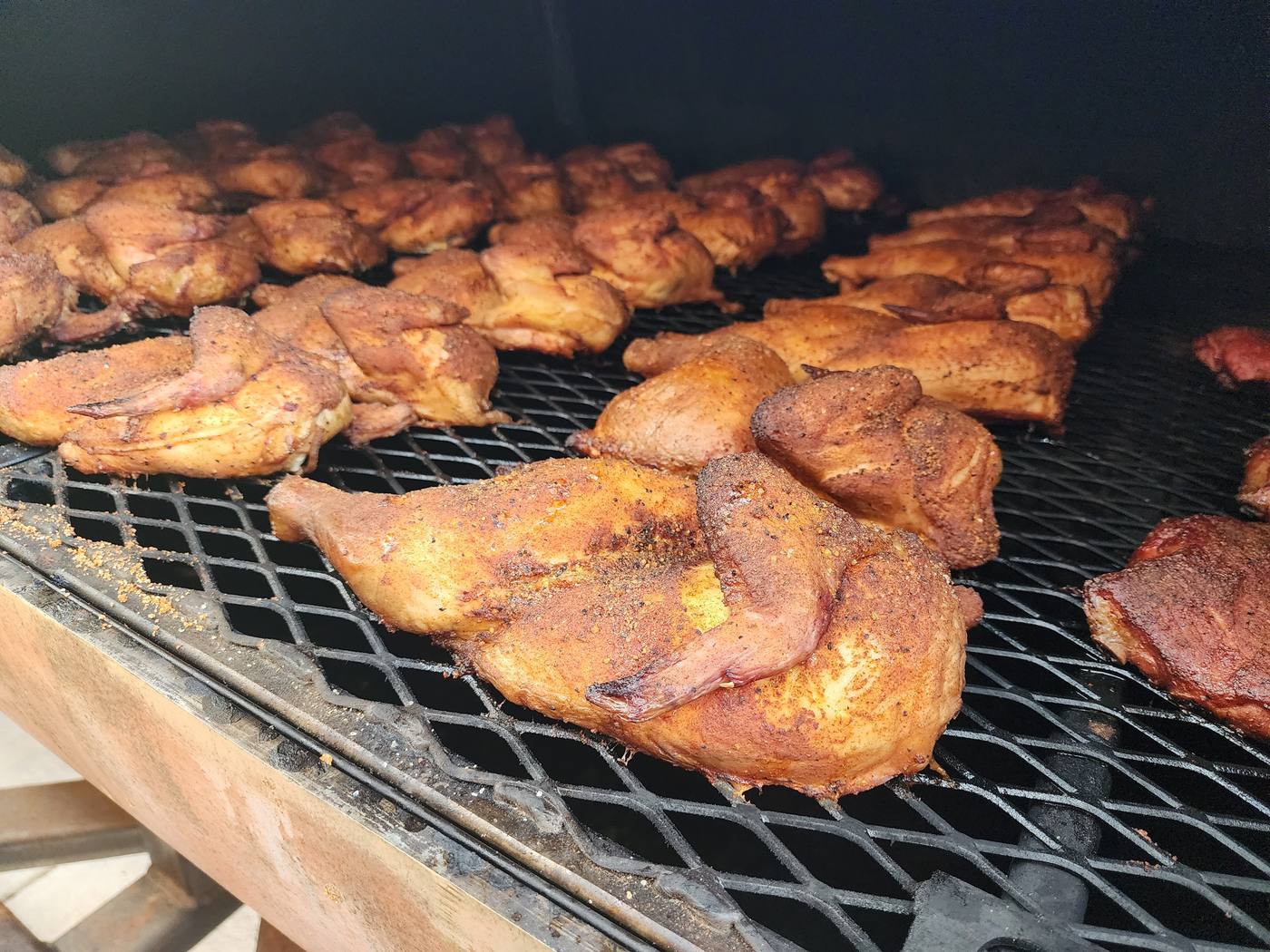 Dozens of seasoned chicken halves laid across a large smoker grate.