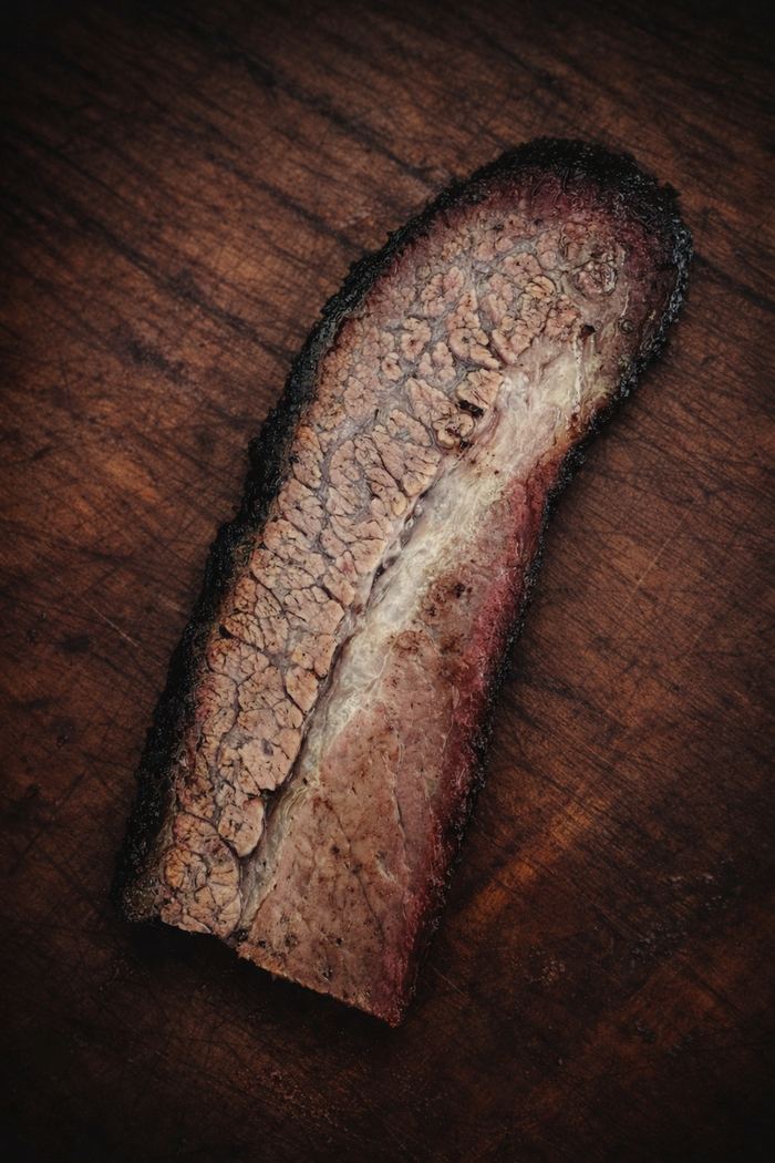 Single slice of finished brisket on a scarred wooden board, bark and smoke ring visible.
